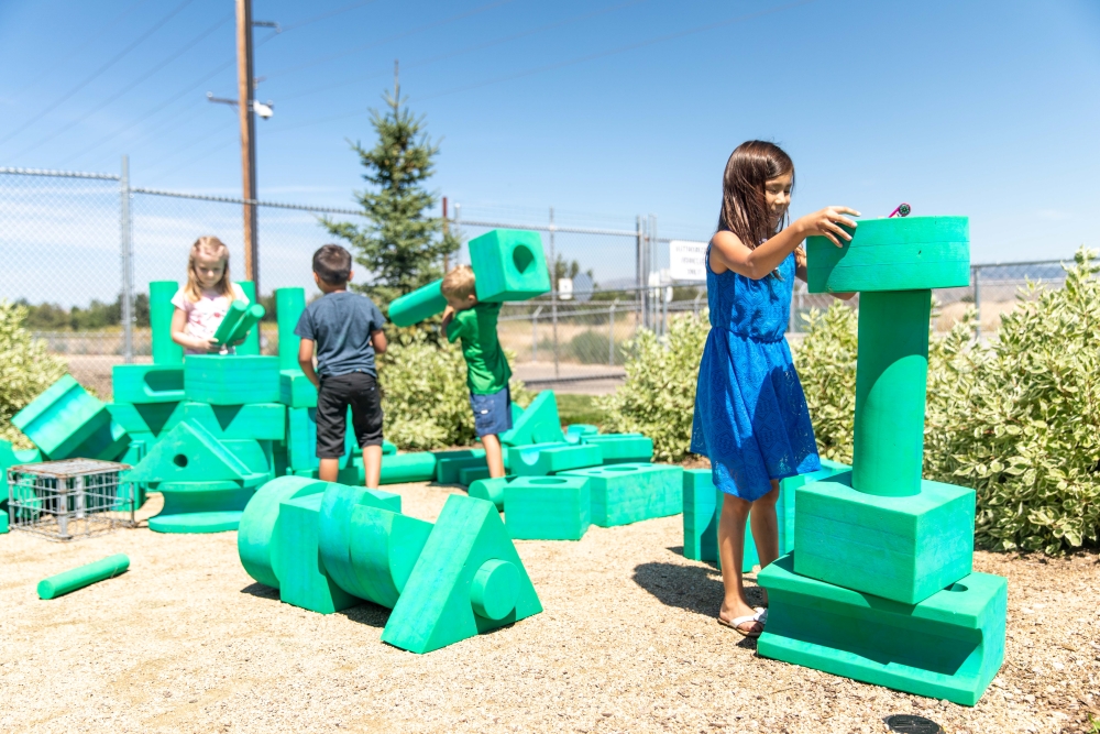 Children in an outdoor location using giant green foam blocks of various shapes to build structures.