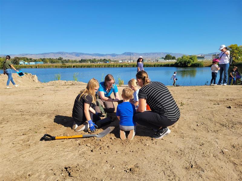 A field scientist presents a sample to students in a dirt field next to the WaterShed reservoir.