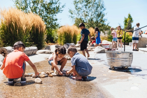 Children playing in The WaterShed's simulated river. Three children in the foreground are arranging rocks to alter the flow of water.